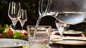 Dricksvatten som hälls ifrån en karaff i ett glas på ett bord dukat till fest.