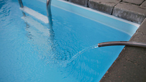 Pool fylls med vatten och vattenslangen ligger &ouml;ver vattenytan.