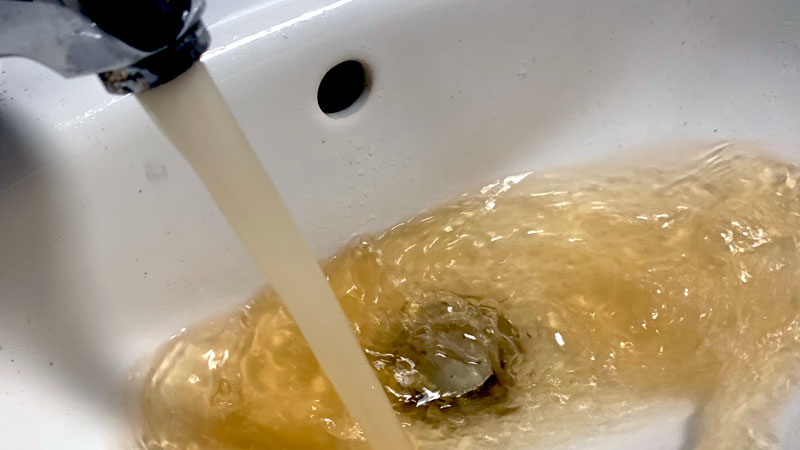 Missfärgat vatten rinner ur en kran och ner i en vask.