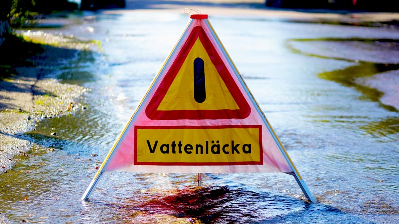 En skylt varnar om en vattenläcka. På marken rinner vatten.